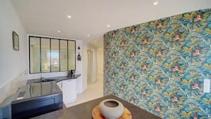 Una cocina moderna con un amplio ventanal, un lavamanos integrado y una pared decorativa con motivos naturales.