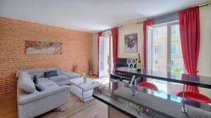 A modern living room with a grey sofa, a white coffee table, and a kitchen area with a black countertop and red chairs. - 3 pi ces Avec Balcon vue sur le Vieux Port A2b022 (Cannes)