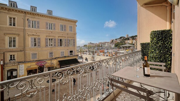 A balcony with a wrought iron railing overlooking a public square with buildings and a hill in the background. - 3 pi ces Avec Balcon vue sur le Vieux Port A2b022 (Cannes)