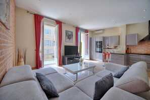 Ein modernes Wohnzimmer mit einer Couch, einem Flachbildfernseher und einer Küche im Hintergrund.