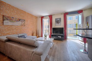 Ein modernes Wohnzimmer mit Backsteinwand, einer großen Couch, einem Flachbildfernseher und einem Balkon mit roten Vorhängen.