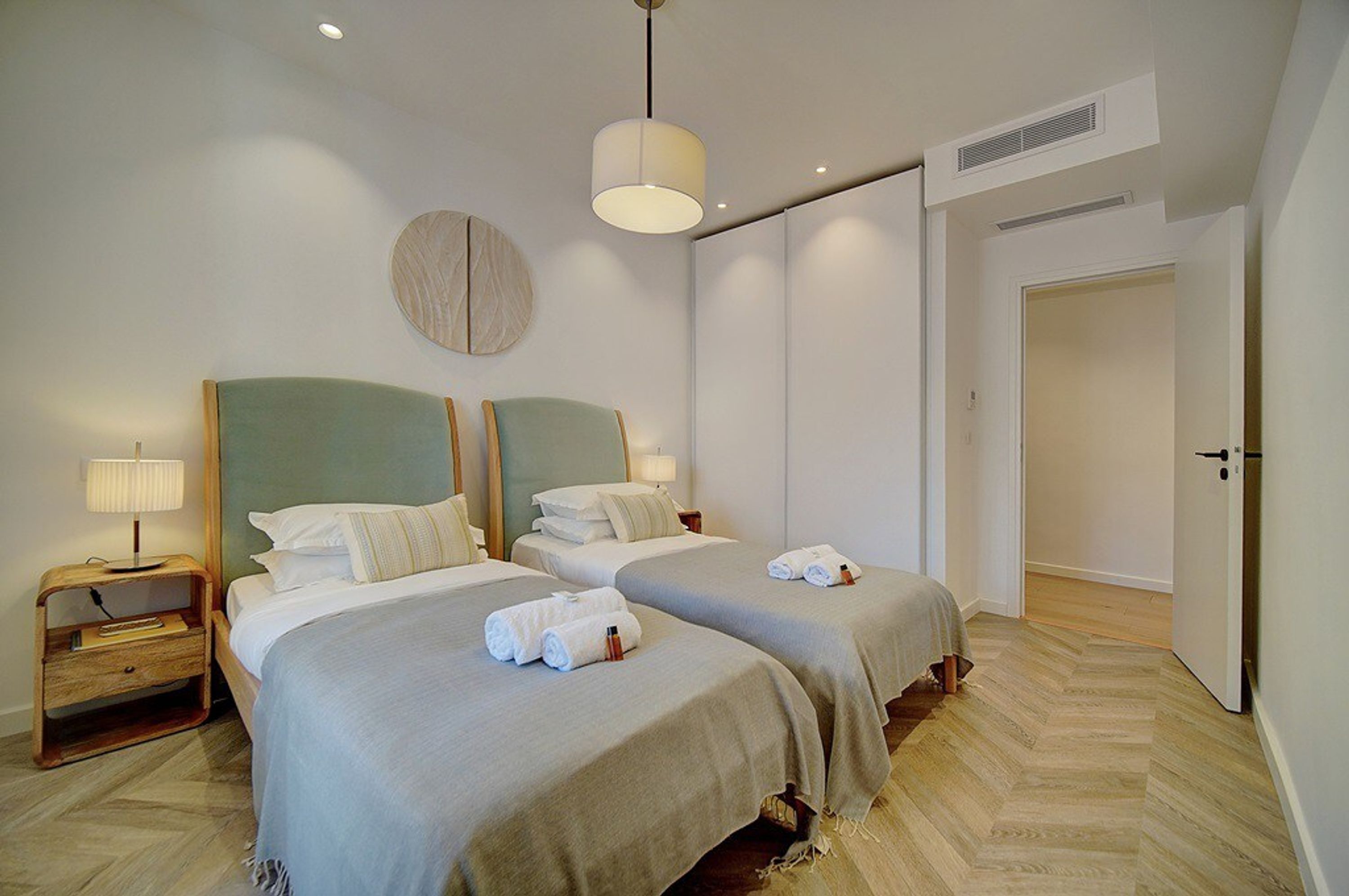 Una habitación de hotel con dos camas, un adorno circular en la pared, una lámpara y una puerta.