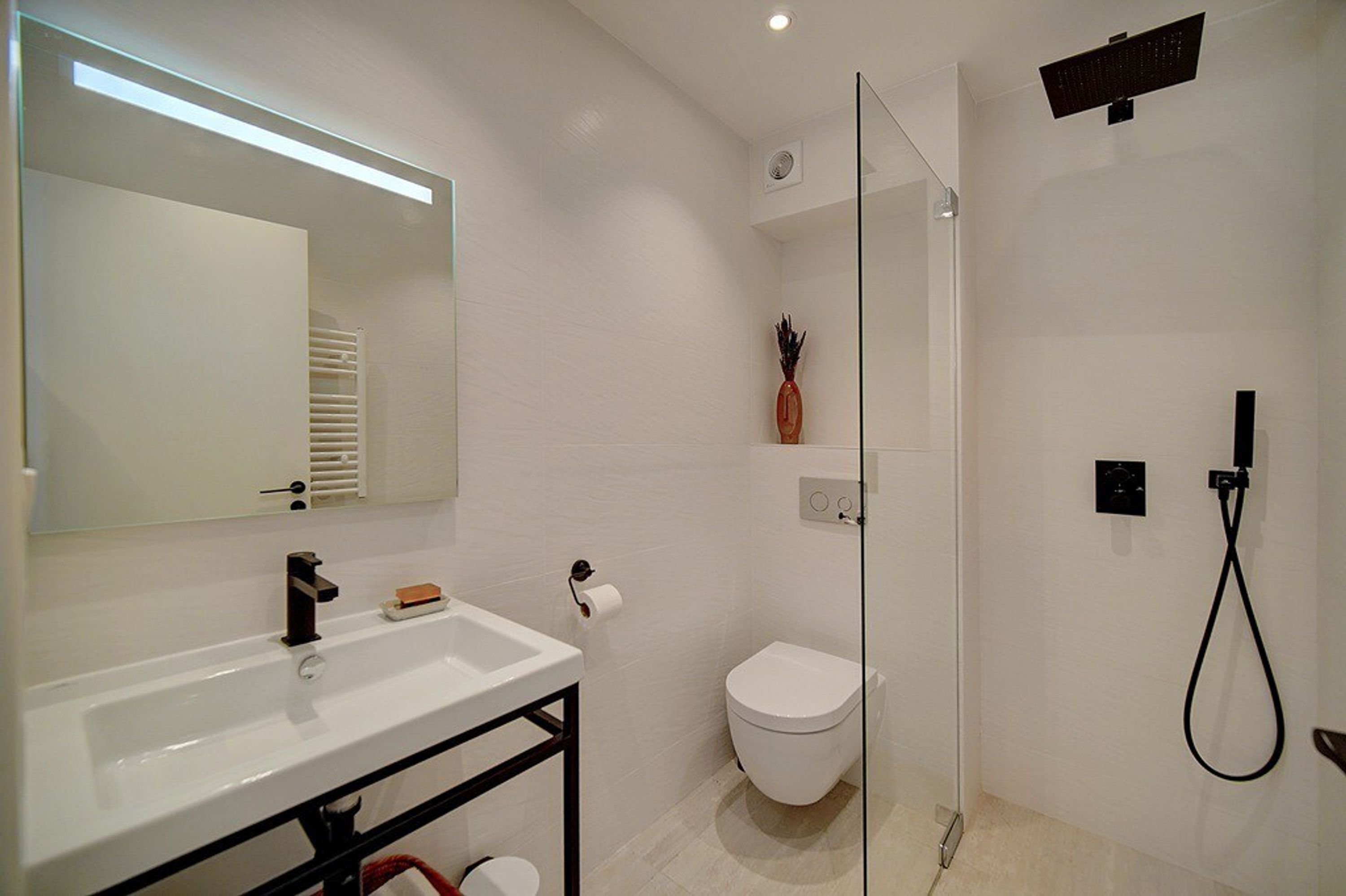 Une salle de bain moderne avec un lavabo blanc, un miroir, des toilettes et une douche à parois de verre.