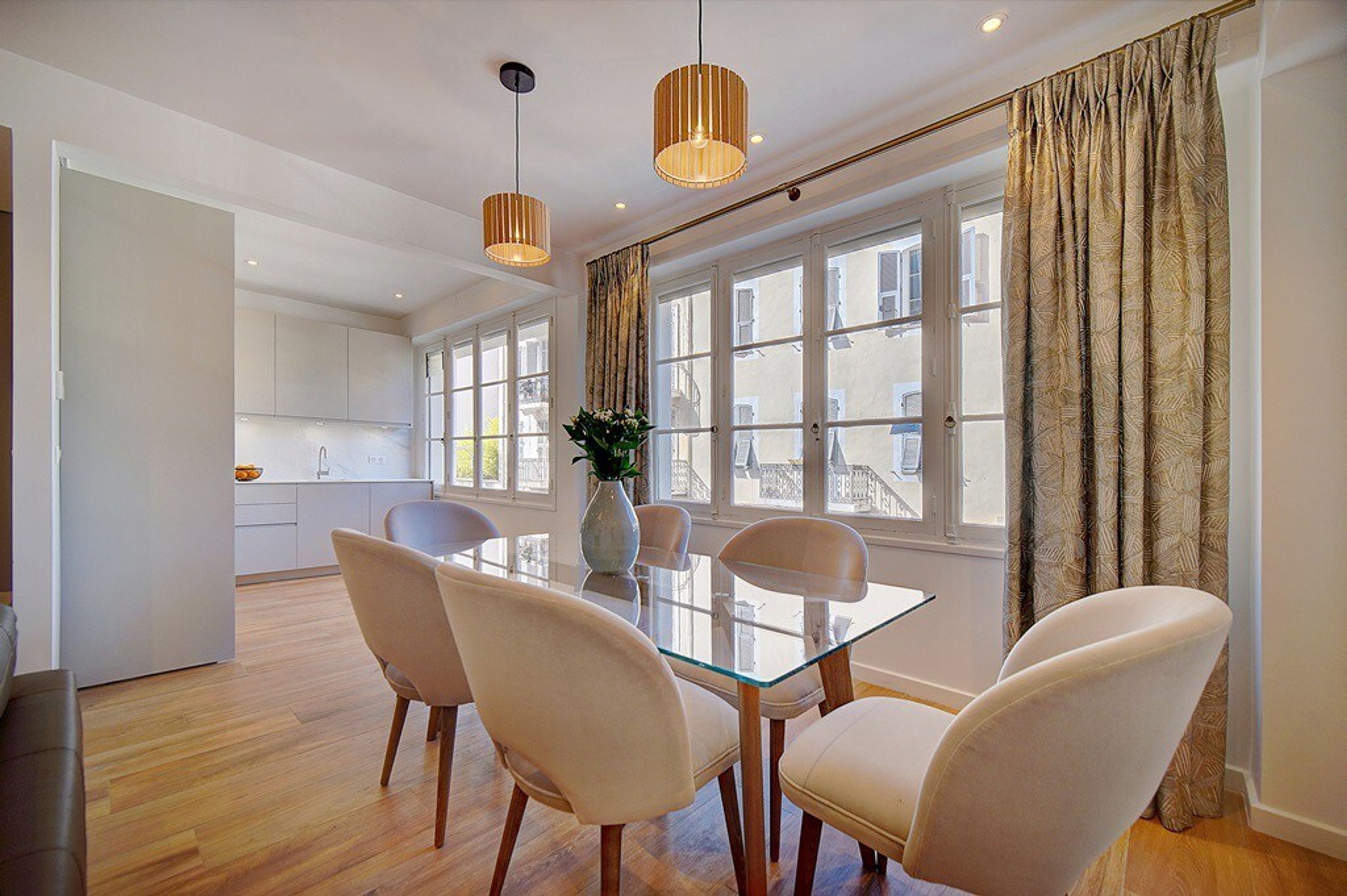 Un comedor moderno con una mesa de vidrio, cuatro sillas y lámparas colgantes.