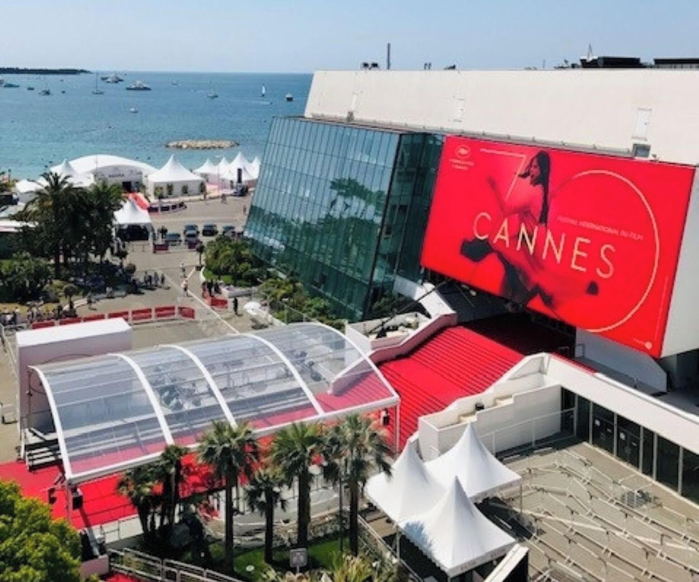 En modern byggnad med en stor, röd skylt med texten ”CANNES”, en glasfasad och en röd matta.