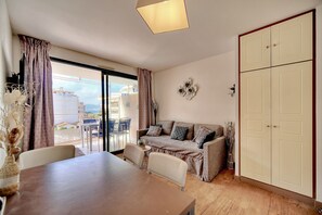 Une pièce comprenant une table à manger, des chaises, un canapé, une armoire et donnant sur l’extérieur grâce à une porte vitrée.