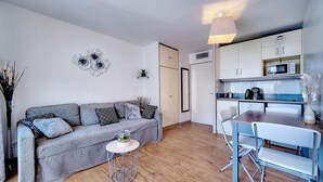 A modern living room with a grey sofa, a small round table, and a dining area with a white table and chairs. - Elegant 2 Pieces Piscine Proche Plages A1b235 (Cannes)