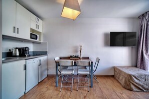Una cocina compacta con electrodomésticos modernos, un comedor con mesa y sillas, un televisor de pantalla plana en la pared y una cama con cabecera.