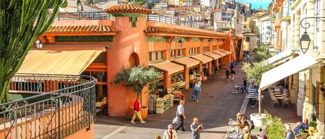 A bustling street with outdoor seating, a market, and a building with a tiled roof.
