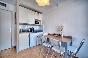 Cocina compacta con armarios blancos, microondas, lavavajillas y una mesa de comedor con sillas.
