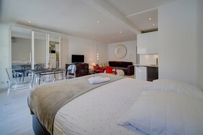 Ein modernes Hotelzimmer mit einem großen Bett, einem Schreibtisch mit Stuhl, einem Fernseher und einer Küchenzeile.