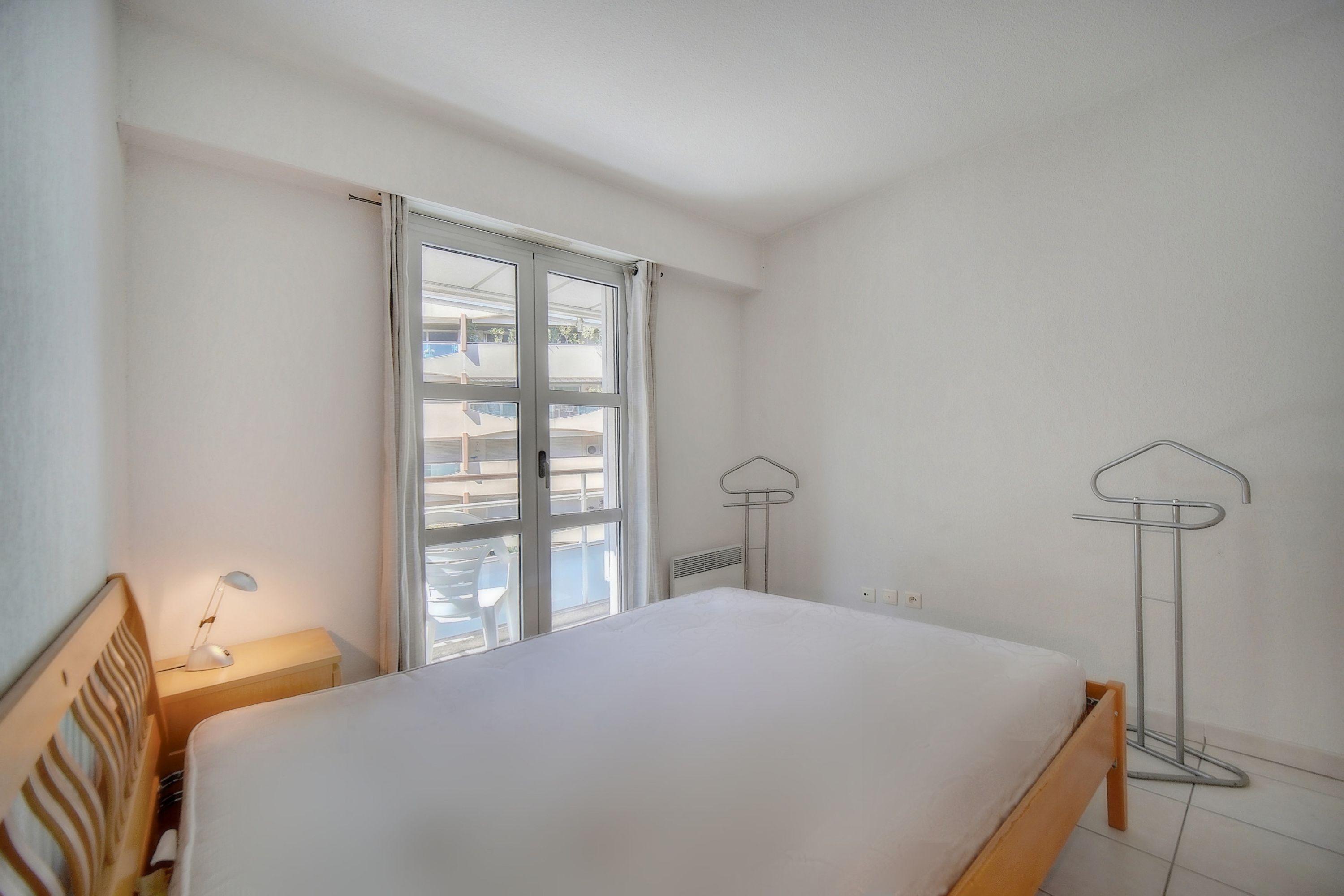 Ein Schlafzimmer mit einem Bett, einem Nachttisch mit Lampe, einem Fenster mit Vorhängen und einer Stehlampe.