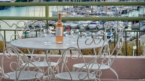 En balkon med et rundt bord og fire stole, ud til en lysthavn med mange både.
