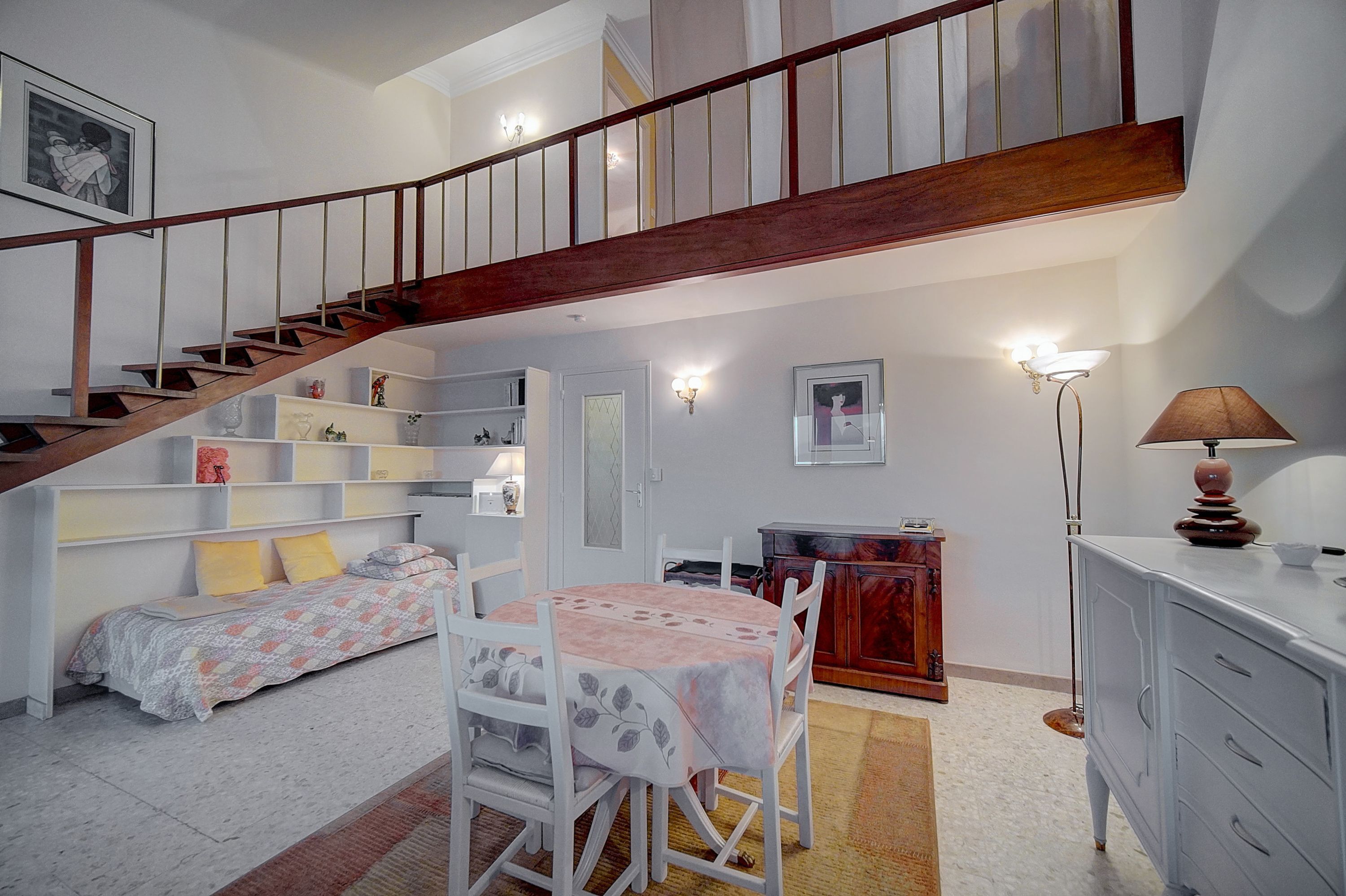 Ein Schlafzimmer mit Bett, Schreibtisch, Stuhl, Kommode, Lampe und einer Treppe.