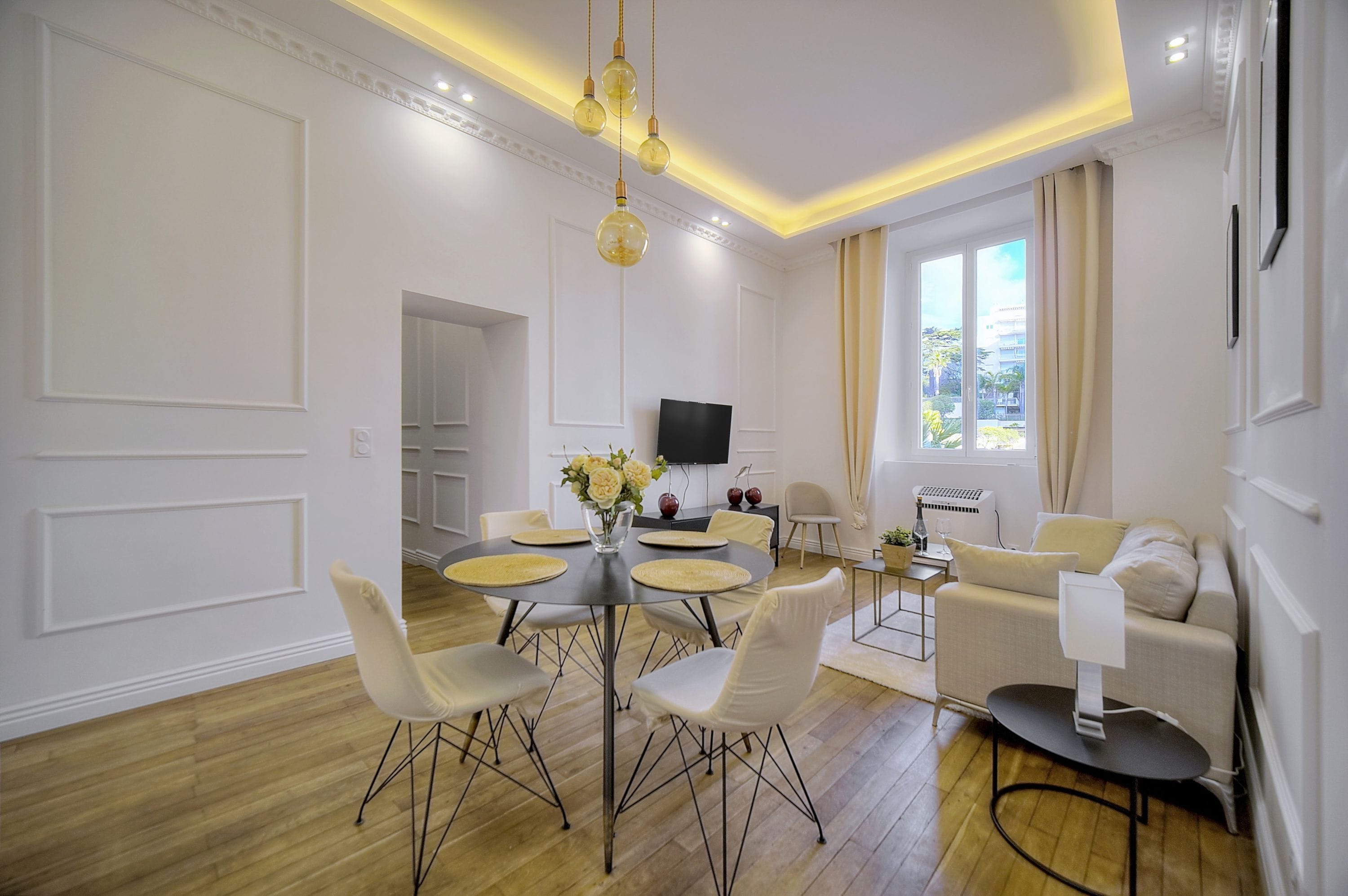 A modern living room with a dining area, a flat-screen TV, and a sofa.
