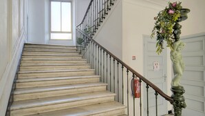 Eine imposante Treppe mit schwarz-weiß kariertem Boden, weißen Wänden und einem grünen Geländer.