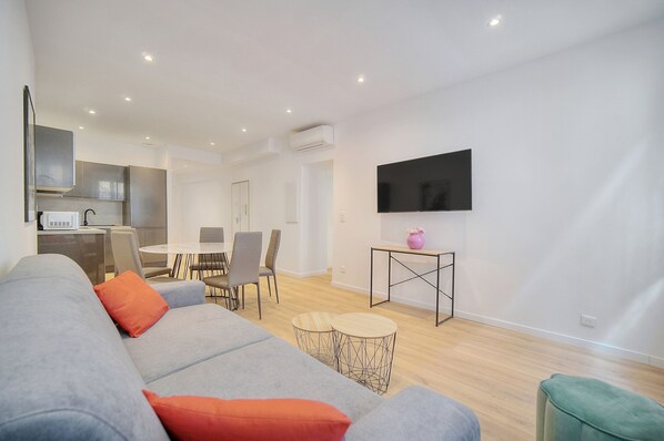 A modern living area with a grey sofa, orange cushions, a dining table with chairs, a TV mounted on the wall, and a small table with a pink vase. - Charmant 3 pi ces Meynadier A2b243 (Cannes)