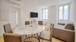 Un salon moderne doté d’une table à manger en marbre, de sièges confortables, d’un téléviseur à écran plat et de grandes fenêtres.