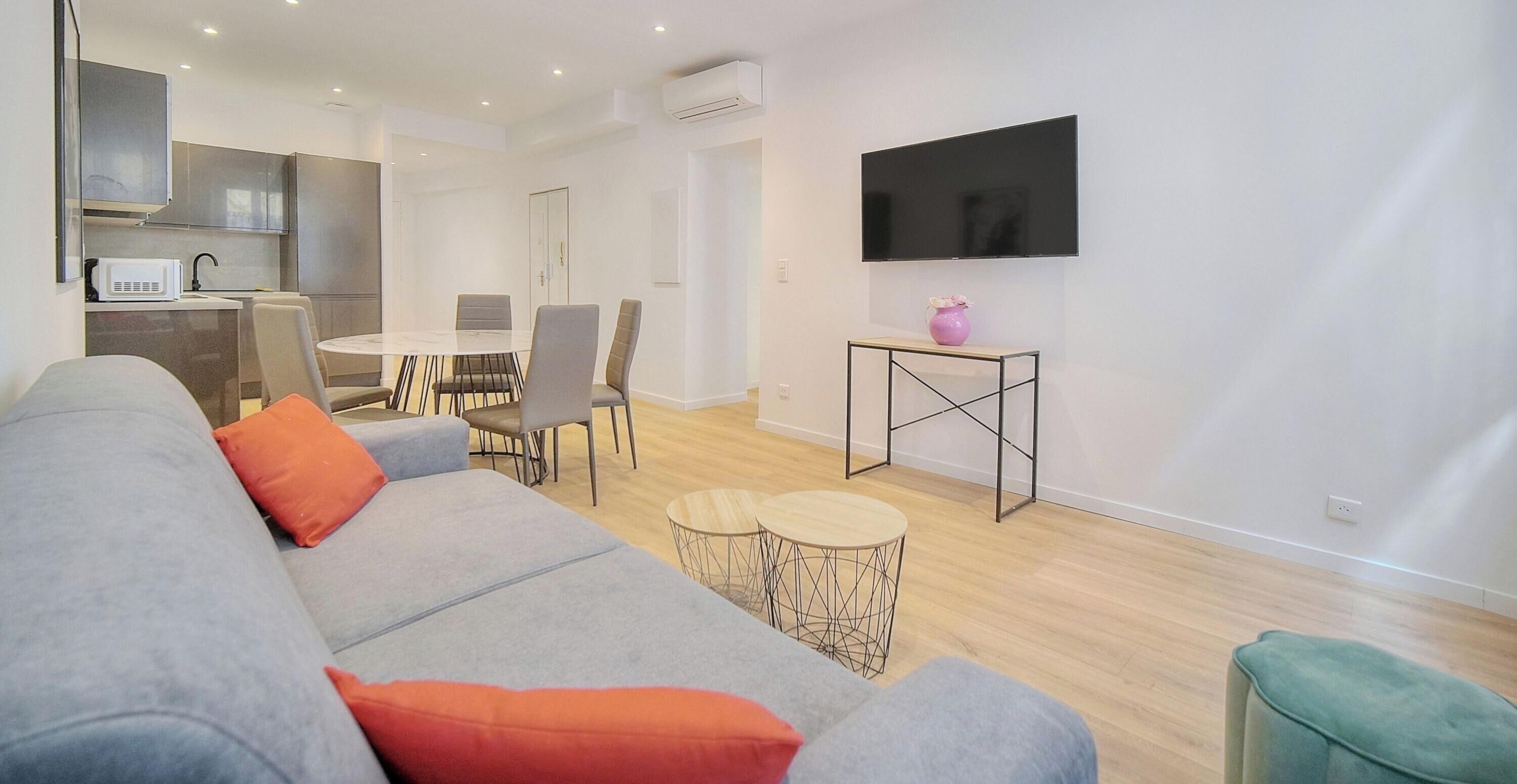 Ein modernes Wohnzimmer mit einem grauen Sofa, einem kleinen runden Tisch und einem an der Wand befestigten Fernseher.