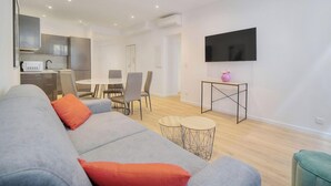 Un salon moderne avec un canapé gris, une petite table ronde et un téléviseur fixé au mur.