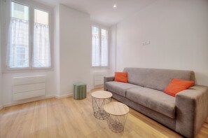 A modern living room with a grey sofa, two round wooden tables, and a green trash bin. - Charmant 3 pi ces Meynadier A2b243 (Cannes)