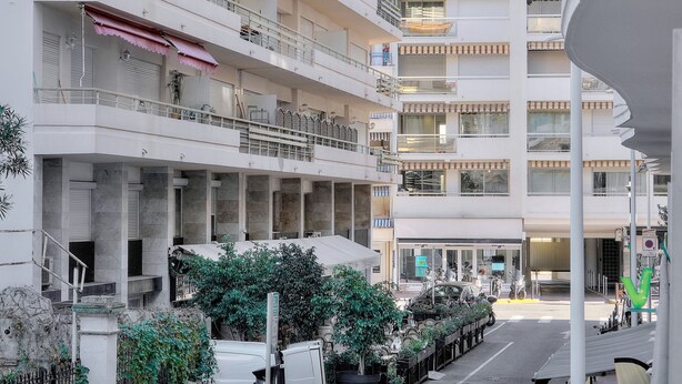 Un immeuble résidentiel à plusieurs étages, doté de balcons, d’une entrée couverte et donnant sur la rue, où l’on peut voir des véhicules garés et de la verdure.