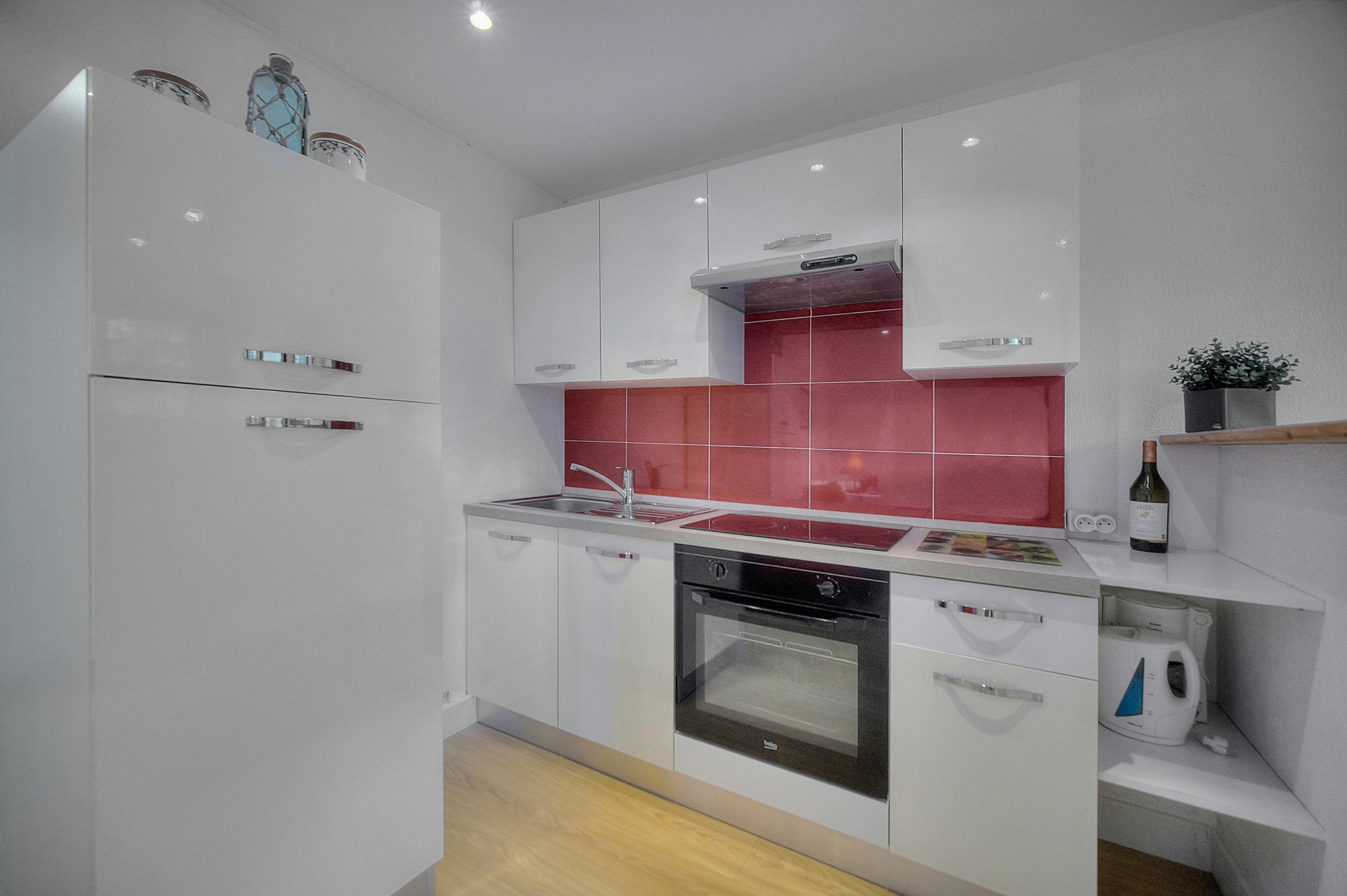 Een moderne keuken met witte kastjes, een rode spatwand en roestvrijstalen apparatuur.