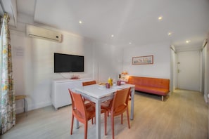 A modern living room with a dining table, orange chairs, a white sofa, a flat-screen TV, and a painting on the wall. - Studio Spacieux 3min Plages Croisette A0b123 (Cannes)