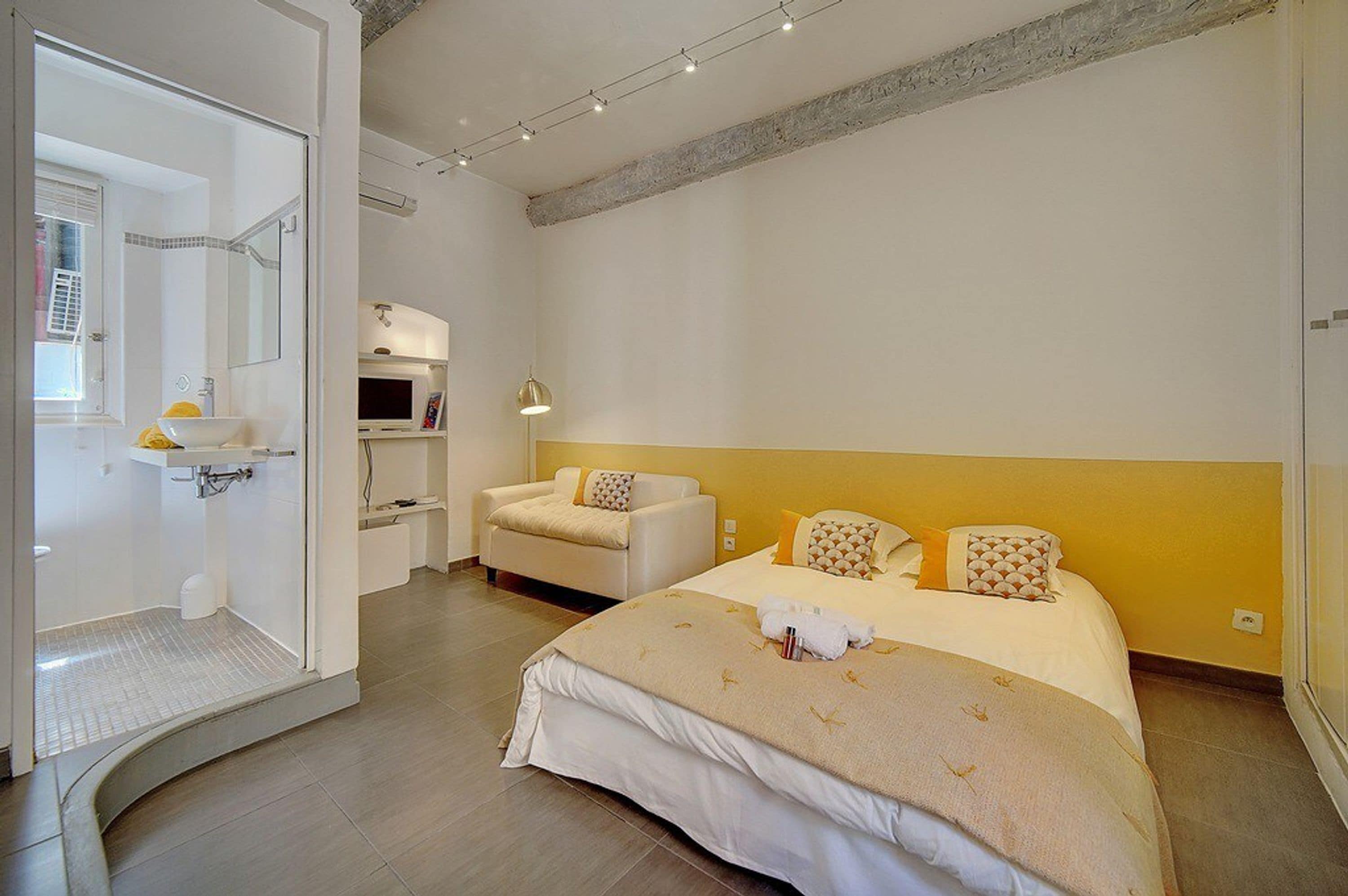 A hotel room with a bed, a sofa, a shower area, and a small kitchenette.