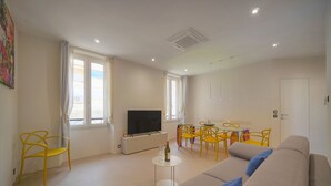 Ein modernes Wohnzimmer mit einer Couch, gelben Sesseln, einem Fernseher und einem kleinen Tisch mit einer Flasche und Gläsern.