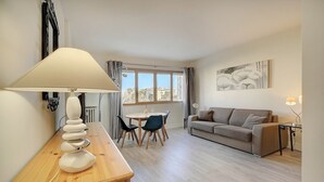 Una sala de estar moderna con un sofá, una mesa de comedor con sillas, una lámpara y un cuadro en la pared.