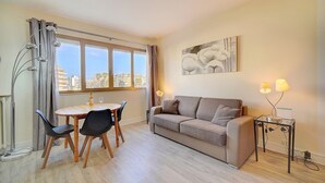 Una sala de estar moderna con un sofá, una mesa de comedor, sillas y un amplio ventanal con cortinas.