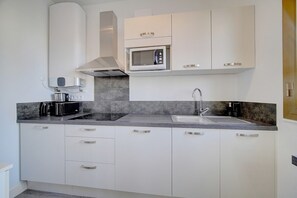 A modern kitchen with white cabinets, a built-in microwave, a gas stove, and a stainless steel sink. - Studio Confortable Calme Proche Croisette A0b107 (Cannes)