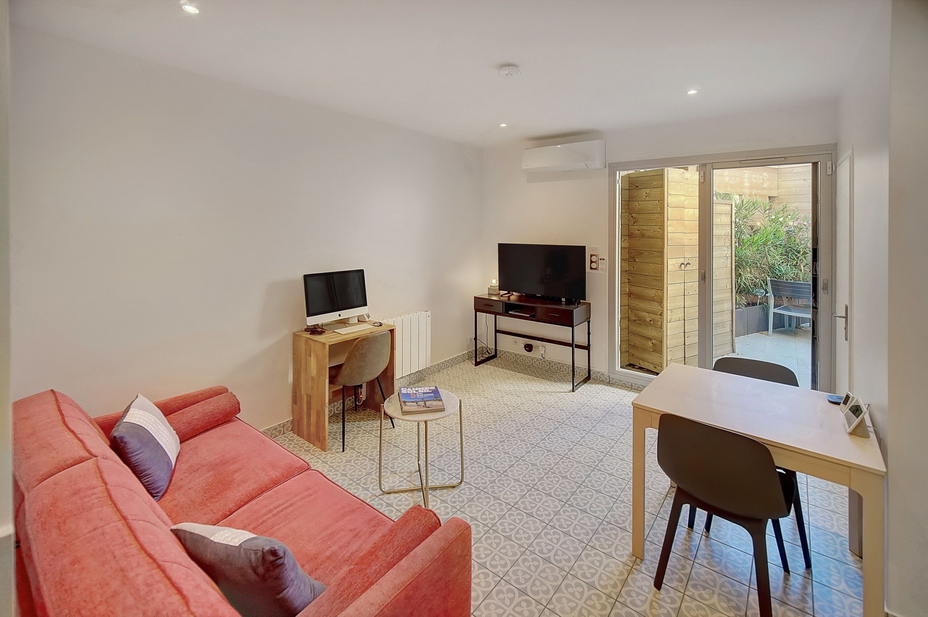 A compact living space with a sofa, a TV on a wooden stand, a small table, and a sliding glass door leading to an outdoor area.