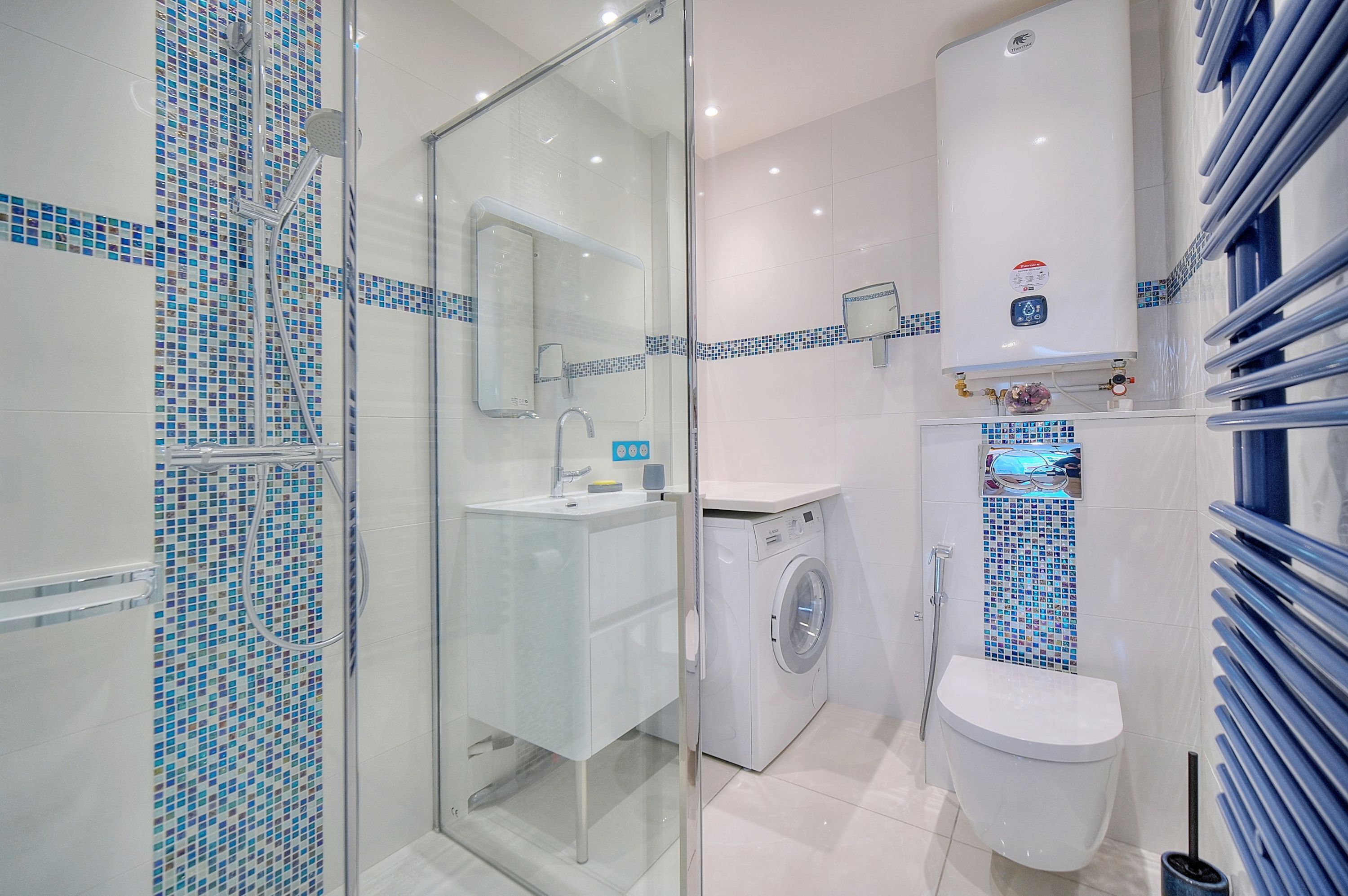 A modern bathroom with a glass-enclosed shower, a washing machine, and a toilet.