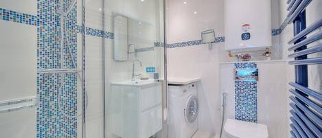 A modern bathroom with a glass-enclosed shower, a washing machine, and a toilet.
