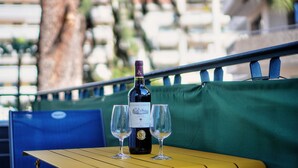 A bottle of Chateau Larroz wine and two glasses on a table with a green cushion and blue railing in the background. - 2 Pieces Moderne 300 m Plages Croisette A1b238 (Cannes)