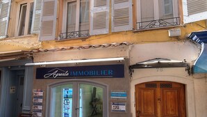 A building with multiple windows and shutters, a storefront with a sign, and a large wooden door. - Charmant 2 Pieces Centre DE Cannes A1b209 (Cannes)