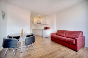 Un salon moderne avec un canapé rouge, une table à manger avec des chaises, et une cuisine en arrière-plan.