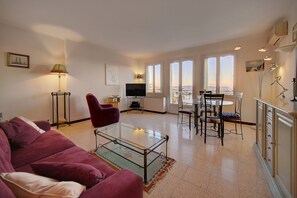 Ein Wohnzimmer mit einem Glastisch, einem roten Sofa, einem Fernseher und einem Essbereich mit Stühlen und einem Tisch.