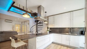 A modern kitchen with white cabinets, a central island with bar stools, a built-in stove, and a staircase leading to an upper level. - Elegant Duplex 5 Chambres Plages DU Midi A5b003 (Cannes)