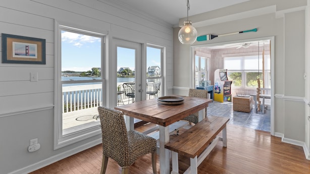 A dining area with a wooden table and chairs, large windows, and a view of the outdoors. - Sounds Right #214-Community pool, private boat dock, kayaks, fish, soundside (North Topsail Beach)