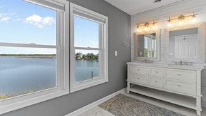 A bathroom with a large window, a white vanity, and a patterned rug. - Sounds Right #214-Community pool, private boat dock, kayaks, fish, soundside (North Topsail Beach)