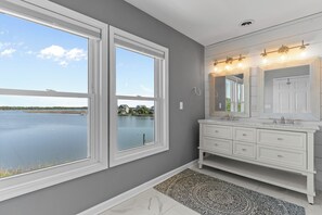 A bathroom with a large window, a white vanity, and a patterned rug. - Sounds Right #214-Community pool, private boat dock, kayaks, fish, soundside (North Topsail Beach)