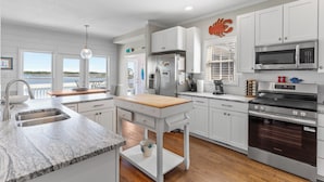 A modern kitchen with white cabinetry, a wooden countertop, a built-in oven, and a view of the outdoors. - Sounds Right #214-Community pool, private boat dock, kayaks, fish, soundside (North Topsail Beach)
