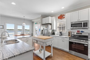 A modern kitchen with white cabinetry, a wooden countertop, a built-in oven, and a view of the outdoors. - Sounds Right #214-Community pool, private boat dock, kayaks, fish, soundside (North Topsail Beach)
