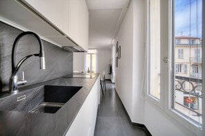 Eine schmale Küche im modernen Design mit einer großen Spüle, einem Edelstahlarmaturen und einem Fenster mit Blick auf eine Straße.