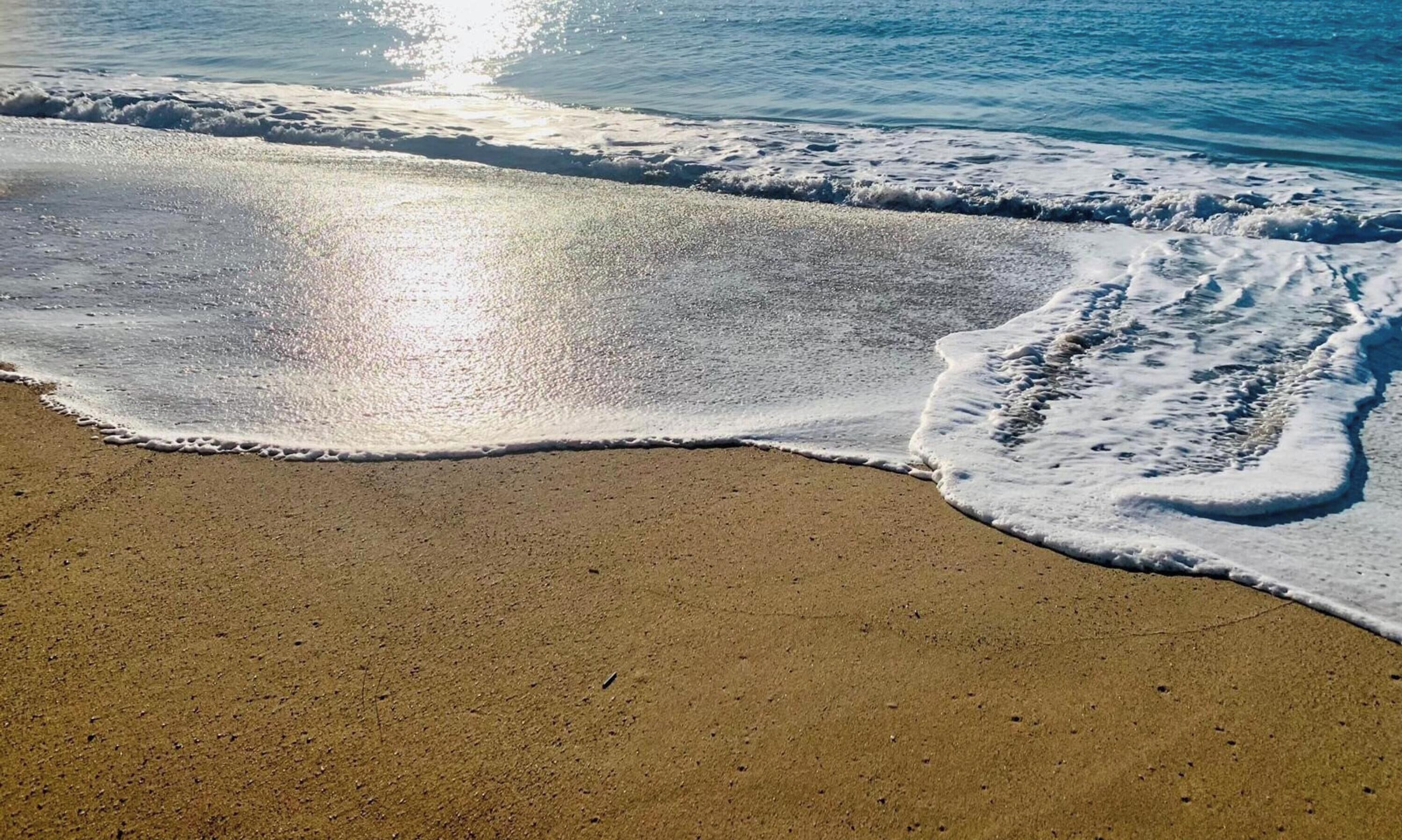 Une plage au sable fin et humide, où de douces vagues viennent lécher le rivage.