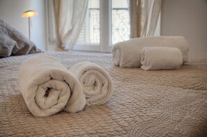 Un letto rifatto con asciugamani bianchi arrotolati e una coperta beige testurizzata.