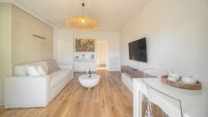 Una sala moderna con sofá, mesa de centro, televisor y un comedor con mesa y sillas de madera.